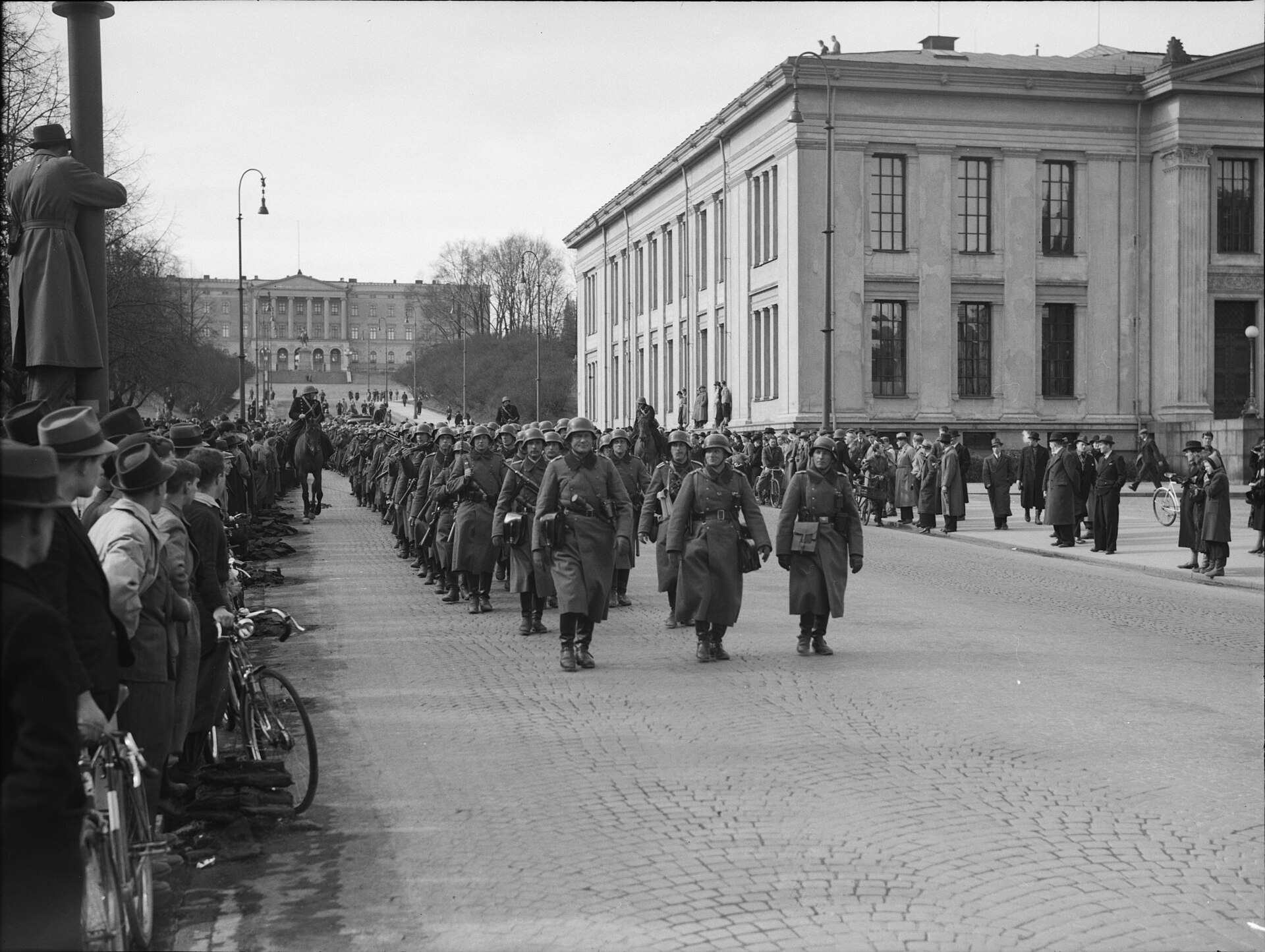 Tyske soldater marsjerer nedover Karl Johans gate i Oslo 9. april 1940. Slottet i bakgrunnen, universitetet til høyre.